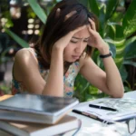 תמונה של בחורה עם ידיים על הראש כאילו מתוסכל יושבת ועל השולחון מחברות וספרים