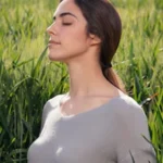 תמונה של בחורה בשדה עוצמת עיניים ונראה כאילו לוקחת נשימה